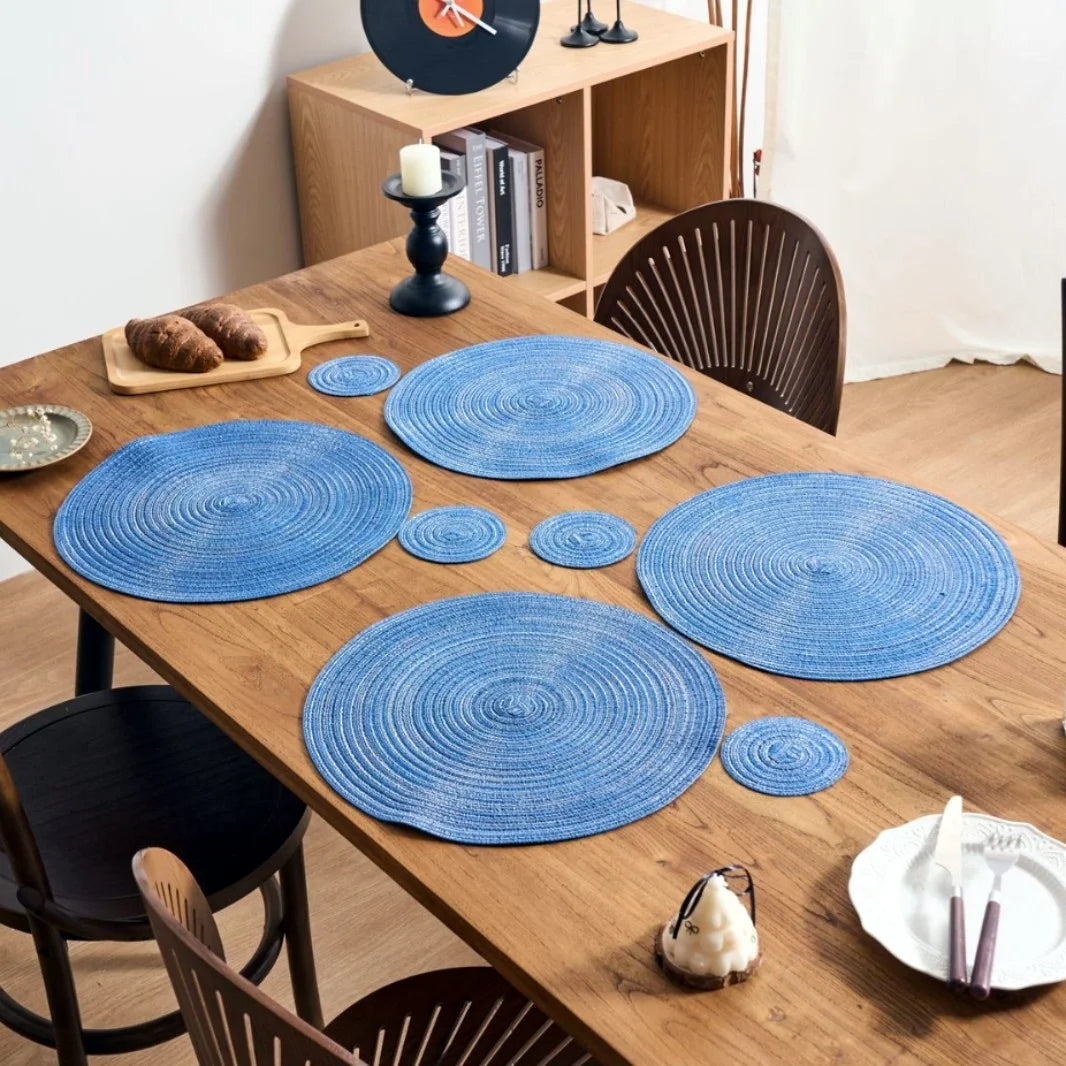 Un ensemble de dessous-de-verre et de sets de table ronds bleus tissés, présentés sur une table en bois.