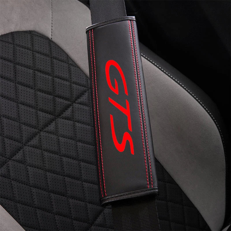 Black seat belt protector cover with red stitching and GTS logo on a gray fabric seat.
