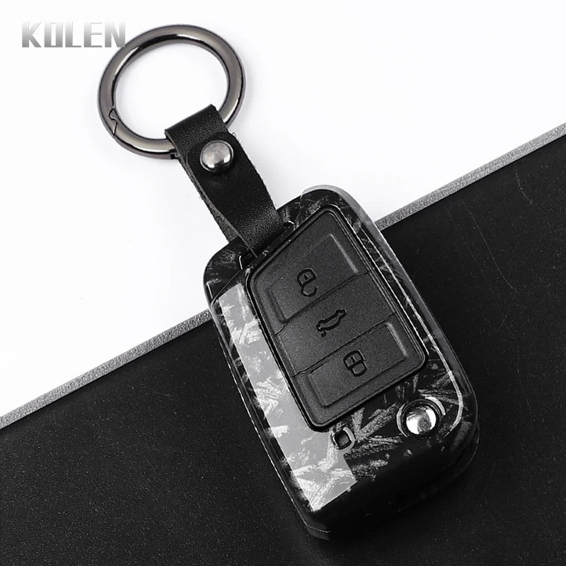 A black carbon fiber button cover for a car key, attached to a metal keyring.