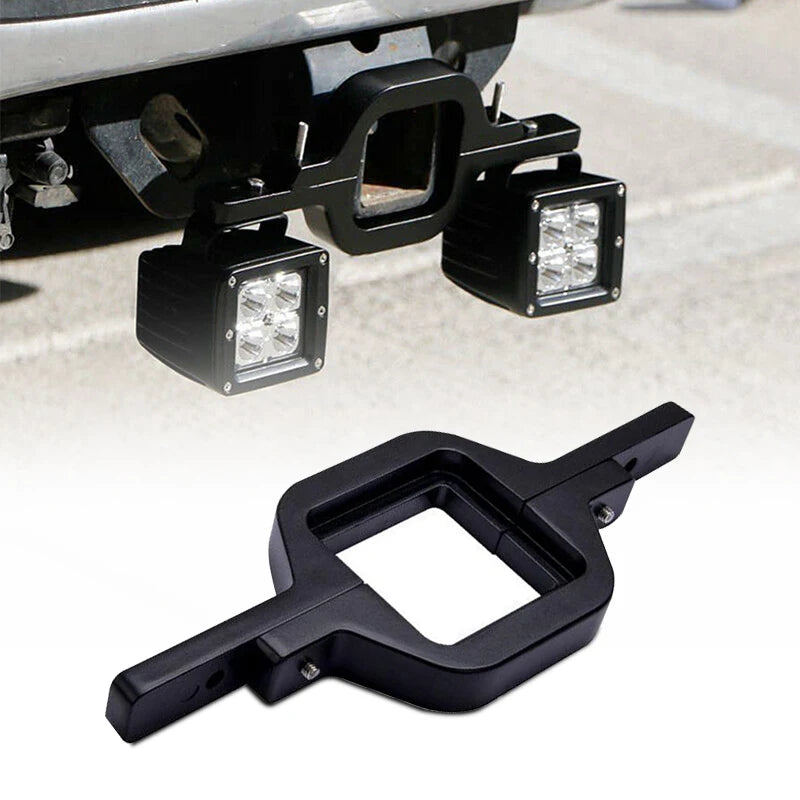 Black dual LED pod mount brackets for a 2.5-inch tow hitch visible on a vehicle frame.