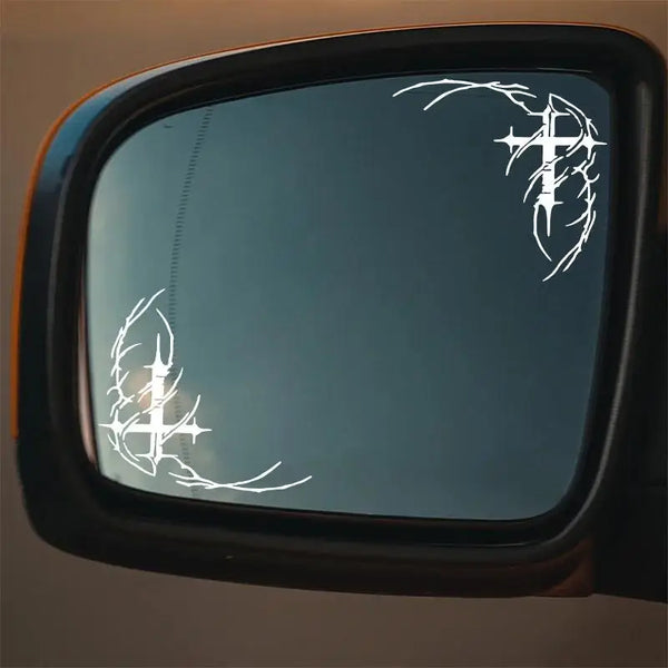 A close-up view of a car window featuring white gothic thorn cross decals.