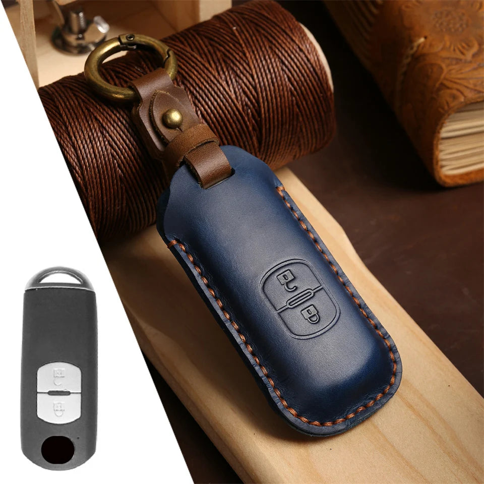 A dark blue leather fob cover with a brass keyring attached, resting on a wooden surface.