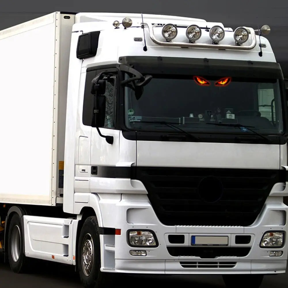 A white truck with aftermarket dynamic demon eye lights installed on the front grille and bumper.
