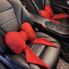 A red bowknot car neck pillow is placed on a black car seat cushion.