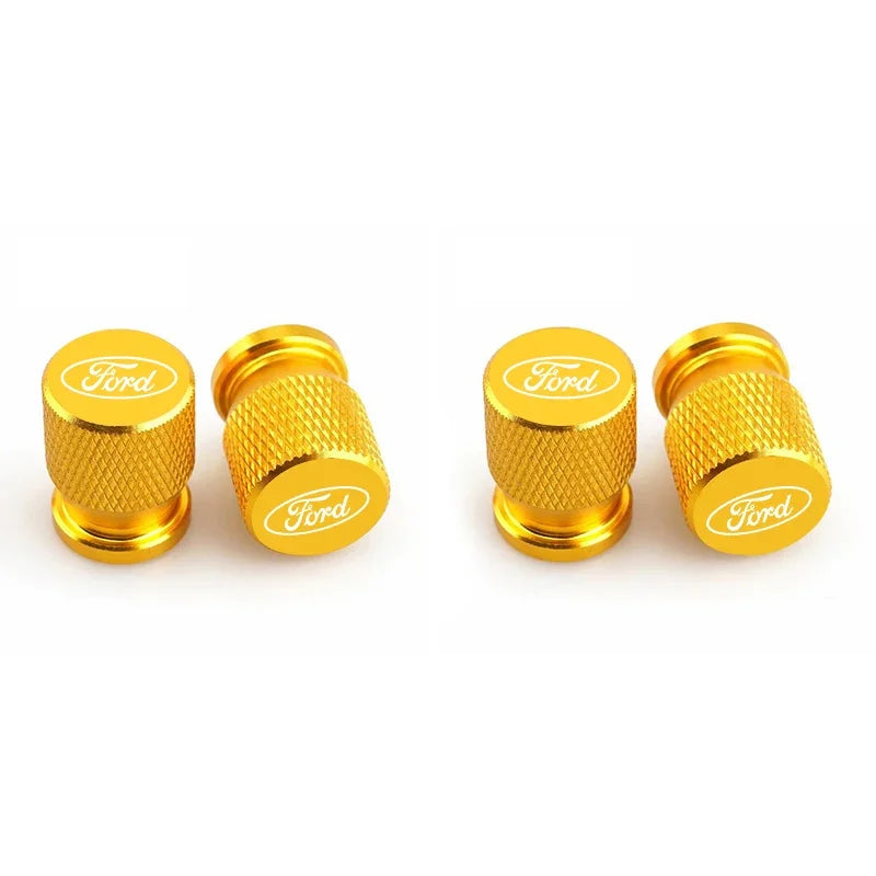 Four gold-colored aluminum car wheel valve caps shown in a row.
