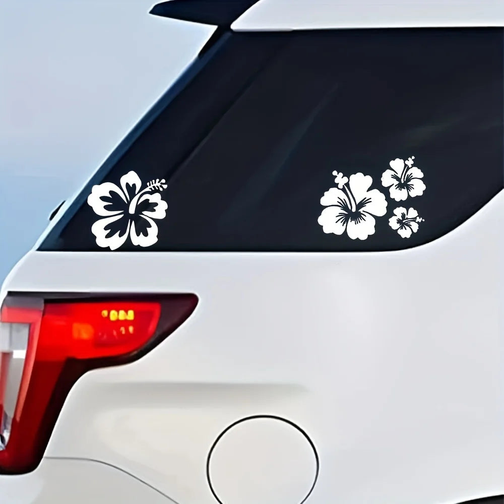 Schwarze Autoschilder mit weißen Hibiskusblüten auf der Heckscheibe eines weißen Fahrzeugs.