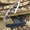 A silver fixed blade knife is shown next to a black leather sheath on a camouflage fabric background.