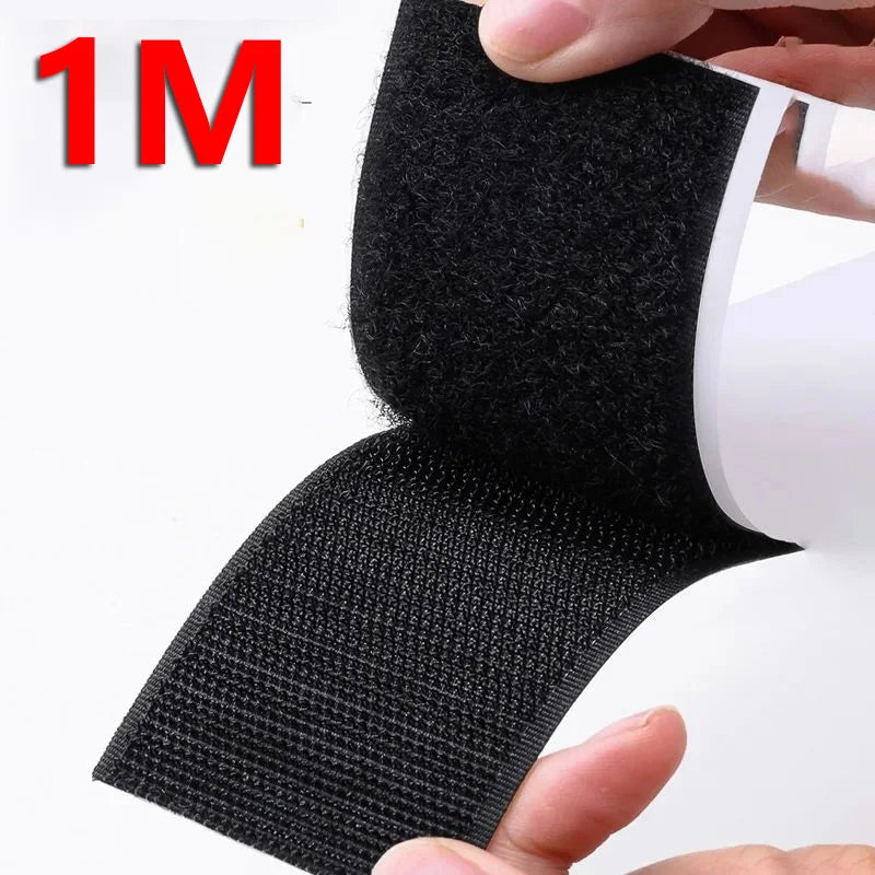 Black hook and loop tape strips being held by a hand, showing the texture and size of the adhesive material.