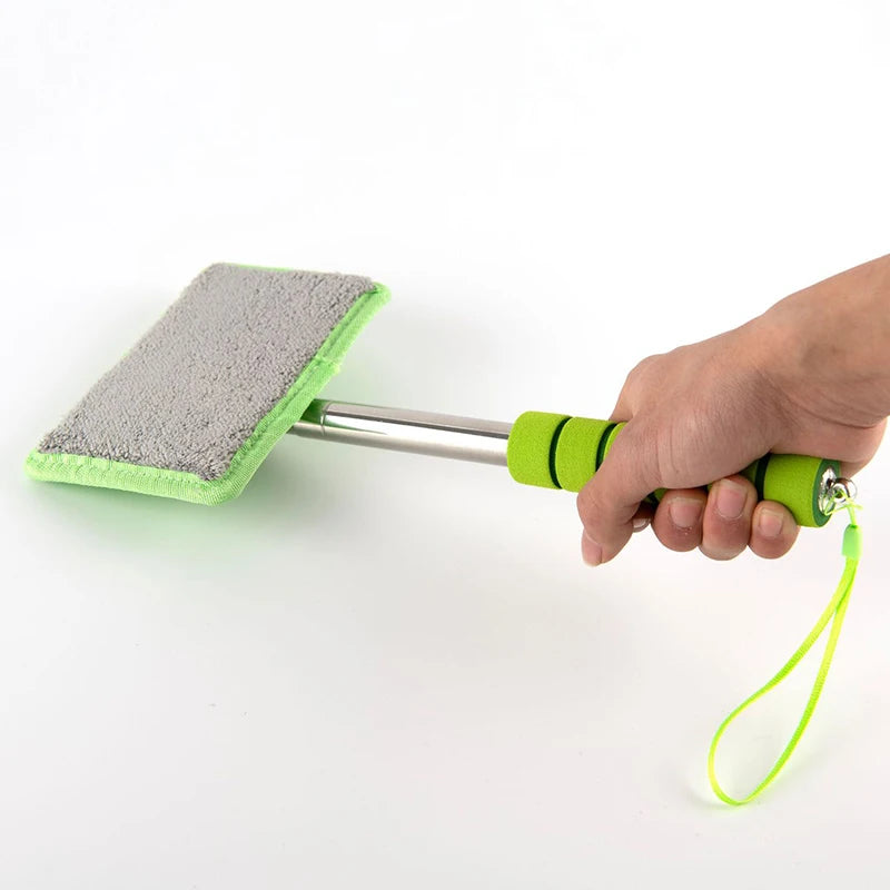 A hand holds a telescopic windshield cleaning brush with a green head and silver handle against a white background.