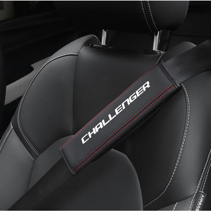 Close-up of a black car seat belt shoulder strap pad with red stitching on a dark gray seat interior.