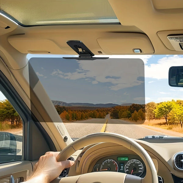 Interior view of a car showing a driver's hand on the steering wheel and a sun visor above the windshield.