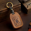 A brown leather key cover with a brass ring and a key silhouette embossed on it, resting on a dark surface.