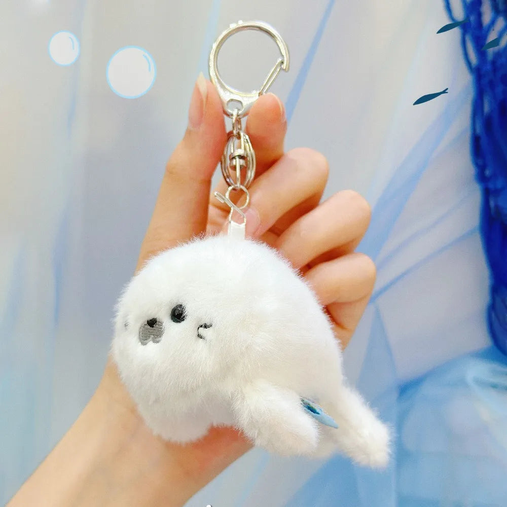 A hand holds a white plush bunny keychain with a gold ring against a light blue background.