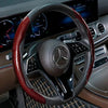 Nahaufnahme eines schwarzen Lenkrads mit roter Kohlefaser-Lederummantelung im Luxusauto-Innenraum.