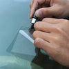 A hand is using a tool from a windshield crack repair kit to apply a substance to the glass.