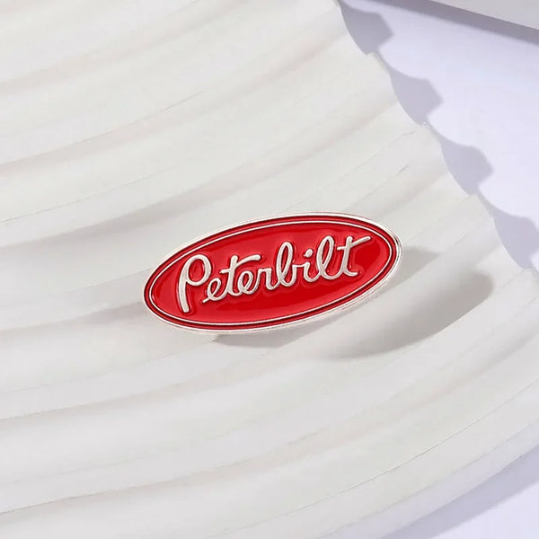 A red oval enamel lapel pin featuring the Peterbilt logo on a white background.