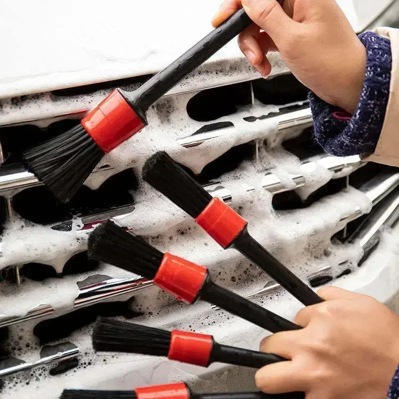 A hand is using a set of black and red detailing brushes inside a car wash machine.