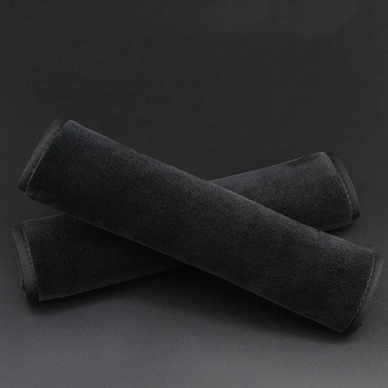 Two black plush seat belt covers lying diagonally on a dark surface.