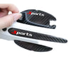 A hand holds a black and carbon fiber car door handle scratch protection kit with the sports logo.