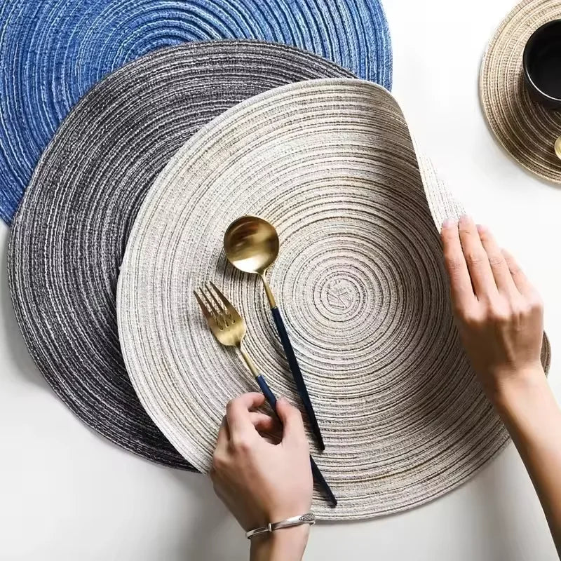 A hand holds a gold spoon above a woven placemat made of gray and beige yarn.