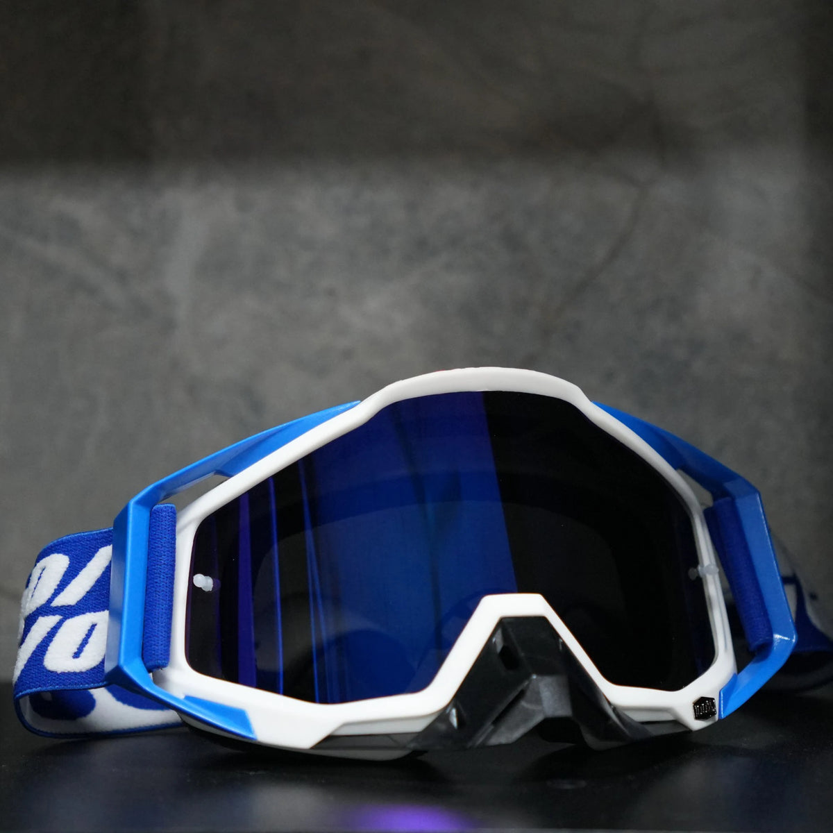 A pair of blue and white high-performance motocross goggles resting on a dark surface.