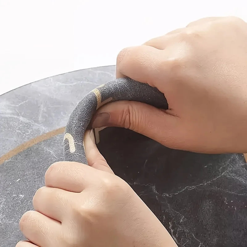 A hand is holding a black pet drinking mat with a gold accent, showing its texture and design.