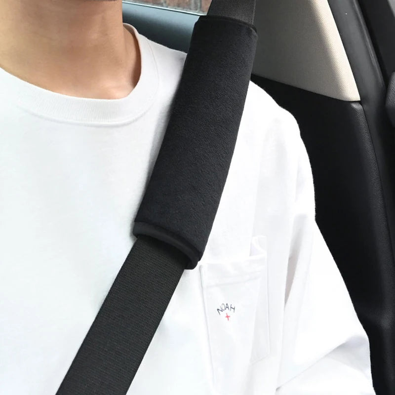 Black dual plush seat belt covers worn over a white shirt in a car interior setting.