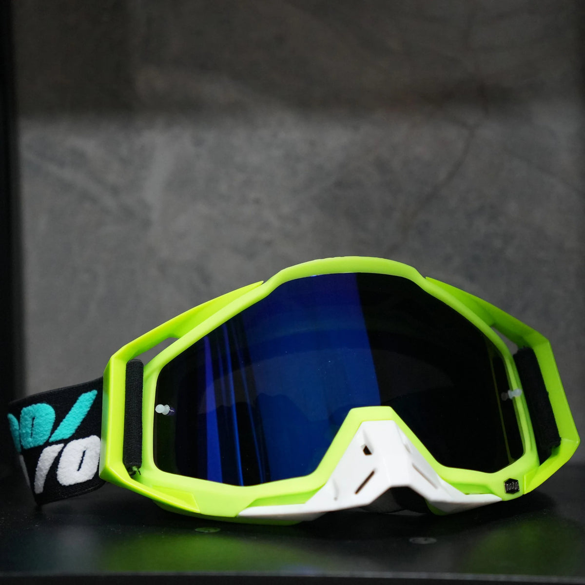 A pair of bright lime green and white high-performance motocross goggles resting on a dark surface.