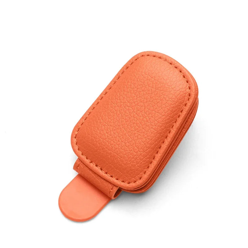 An orange magnetic leather sunglasses holder designed for car sun visors.