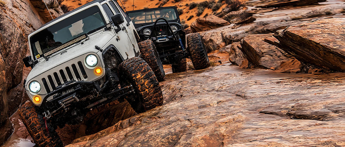 A Jeep Wrangler is driving off-road over rocky terrain, showcasing a rugged vehicle in an arid landscape.