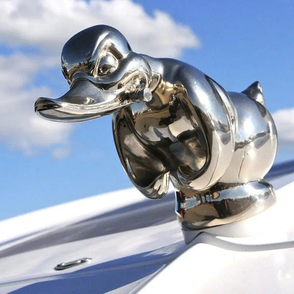 A chrome decorative angry duck hood ornament mounted on a white car surface.