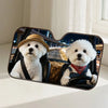 Two white dogs wearing hats and collars sitting in a car windshield sunshade