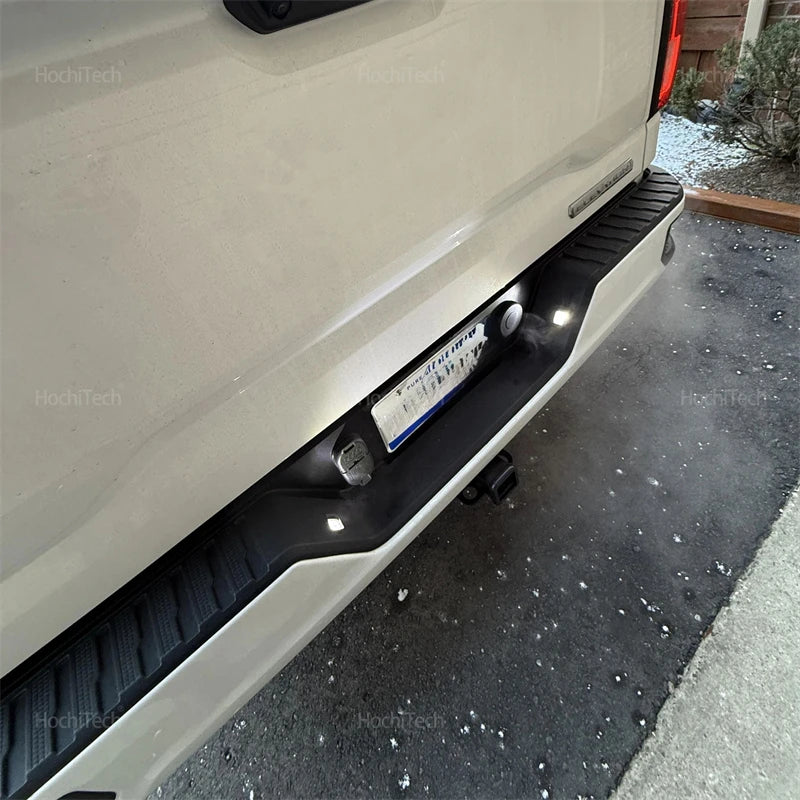 Close-up view of LED license plate lights installed on the lower bumper of a white truck.