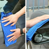 A hand is using a blue microfiber car cleaning cloth to wipe a car surface.