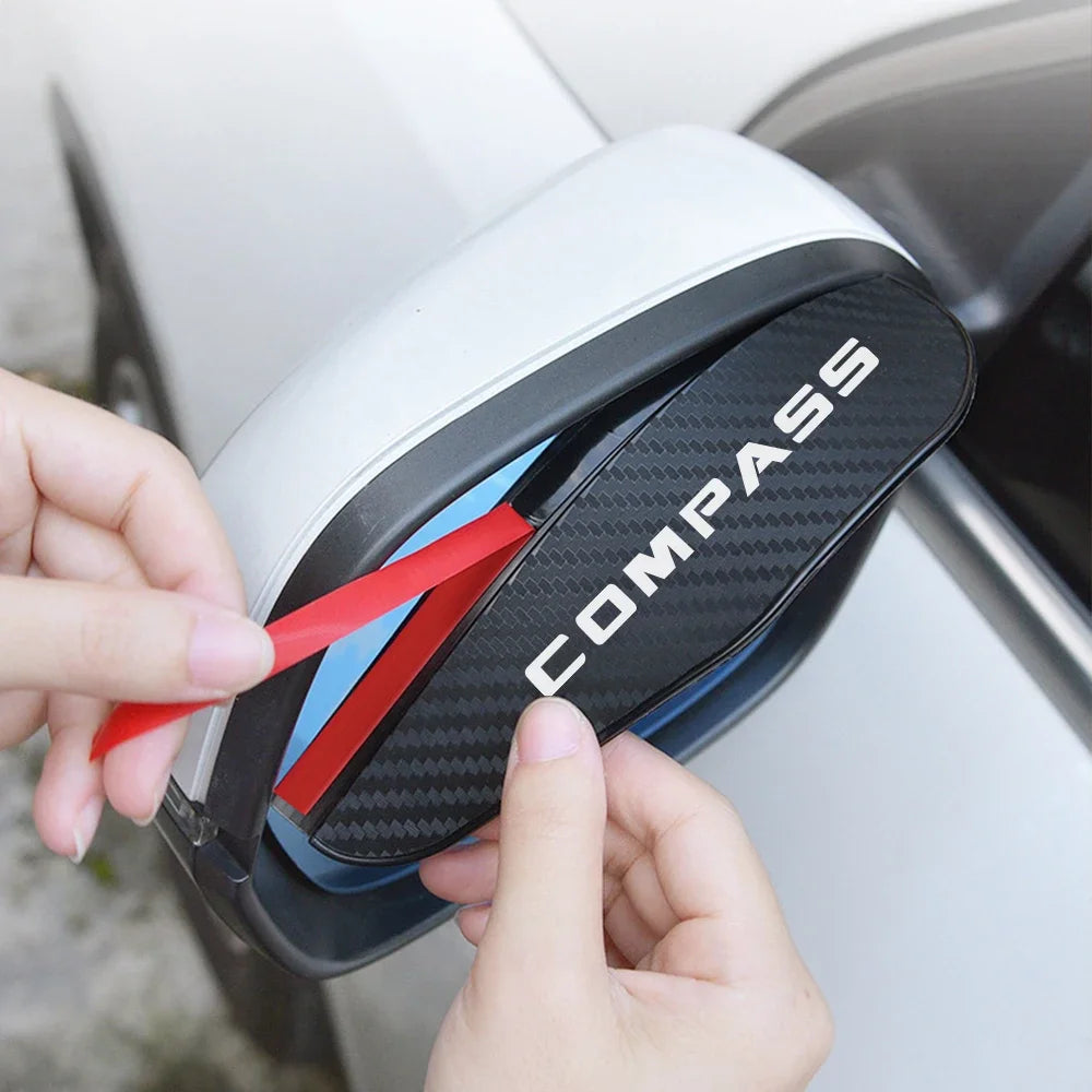 A hand is holding a black carbon fiber texture rain visor for a rearview mirror.