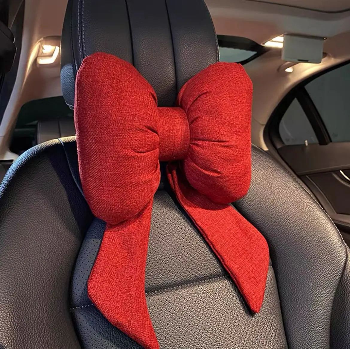 Un nœud en tissu rouge sert d'oreiller de cou placé sur un dossier de voiture sombre.