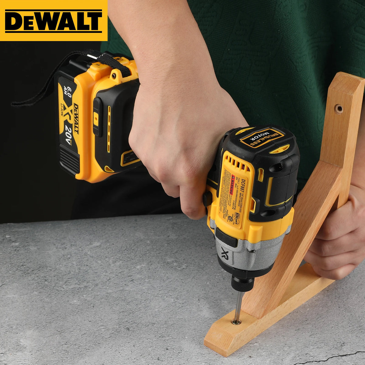 Une main utilise une perceuse sans fil Dewalt 20V jaune et noir pour visser une vis dans un morceau de bois.