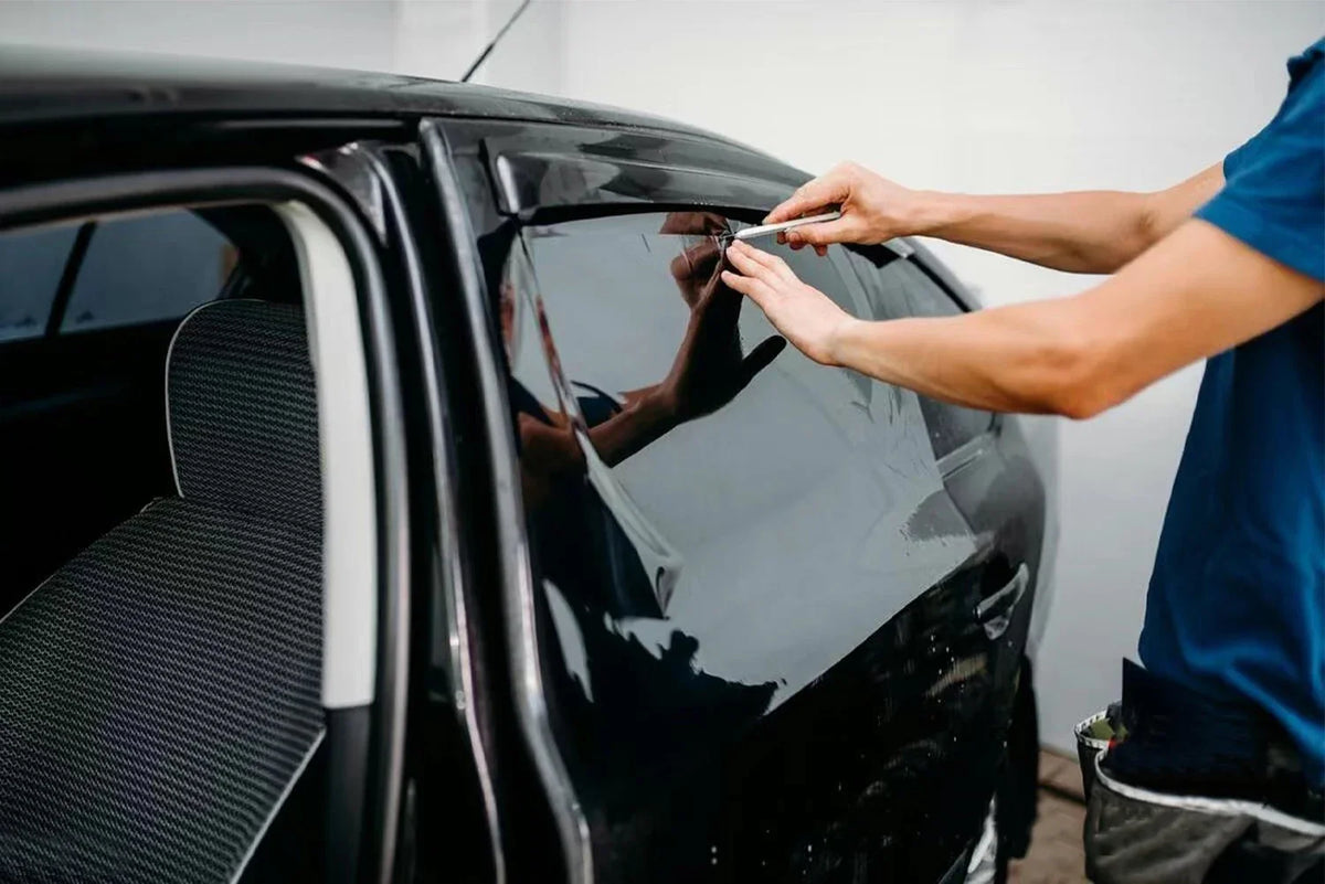 A person applies a car window privacy film to a dark-colored vehicle.