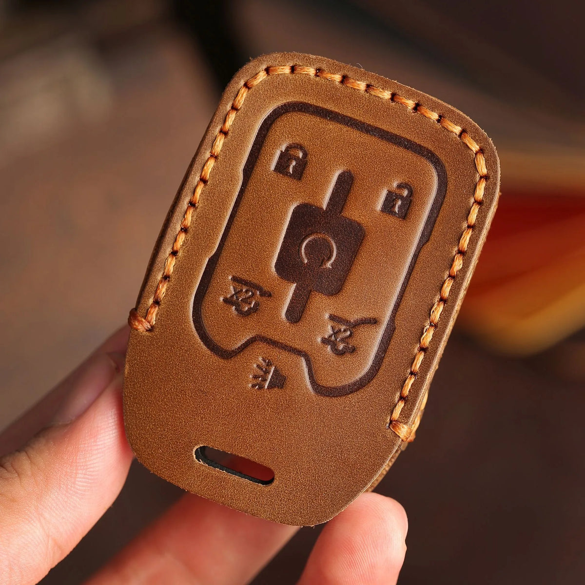 A brown leather key cover with stitching and a cutout for a key is held in a hand.