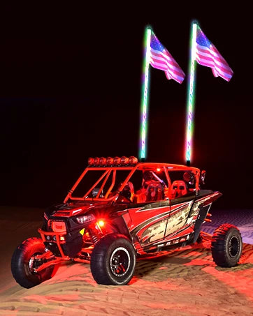 A red UTV is shown with light bar mounting brackets and American flags on poles, parked on reddish sand.