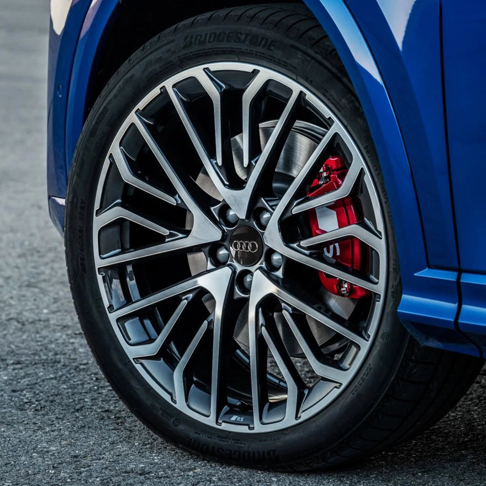 Primer plano de una rueda de coche azul con tapacubos decorativos negros y plateados y una pinza de freno roja.