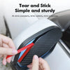 Hands are tearing a red piece of carbon fiber material from a black rain shield for a car rearview mirror.