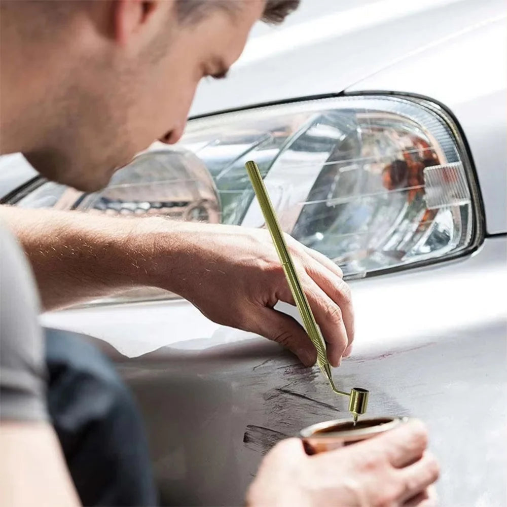 A person uses a precision car scratch repair pen with a fine tip applicator to fix damage on a car's body.