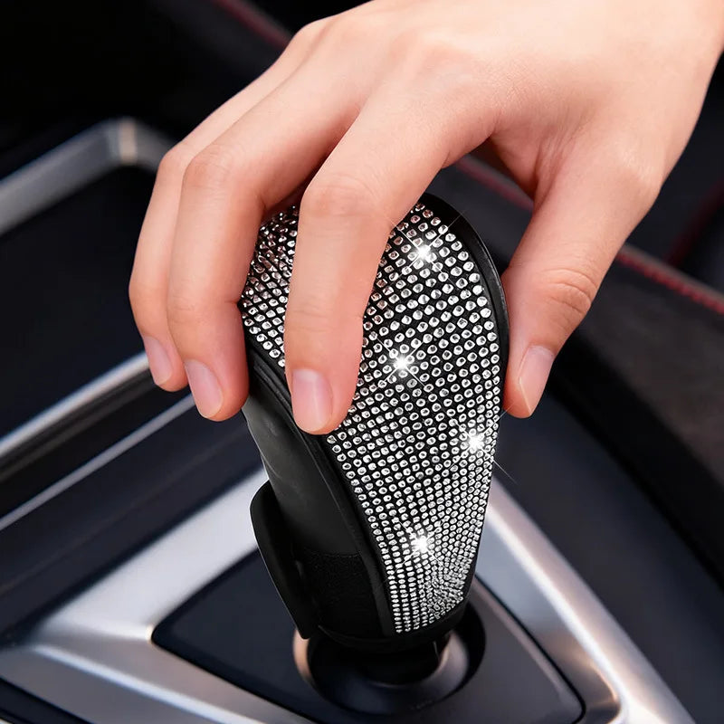 A hand is holding a black gear shift knob cover with sparkling rhinestone detailing.