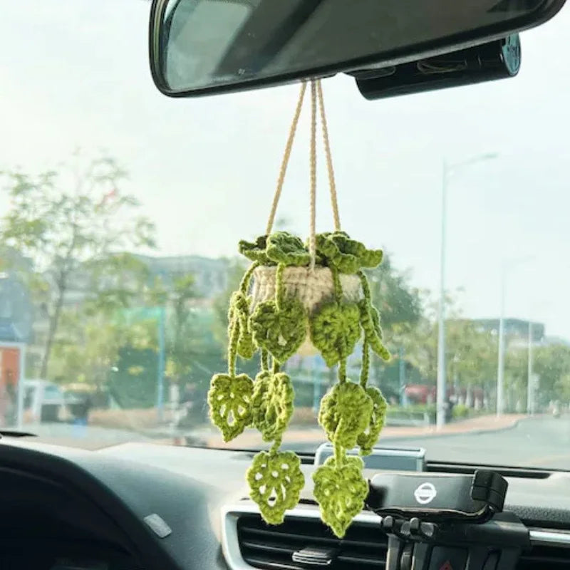 A string of green strawberry crochet decorations hangs from a rearview mirror inside a car.
