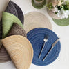 A collection of round placemats in various shades of green, beige, and blue woven from cotton yarn.