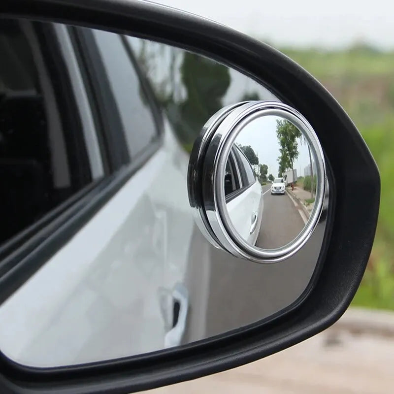 A close-up view of a silver dual-lens car blind spot mirror mounted on a black vehicle door.