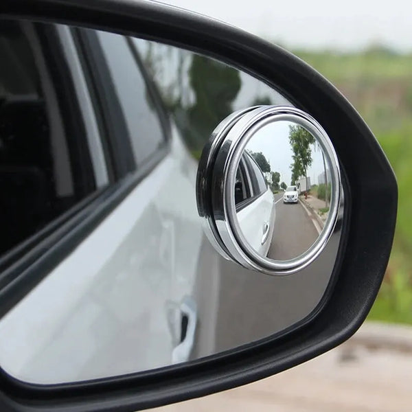 A close-up view of a silver dual-lens car blind spot mirror mounted on a black vehicle door.