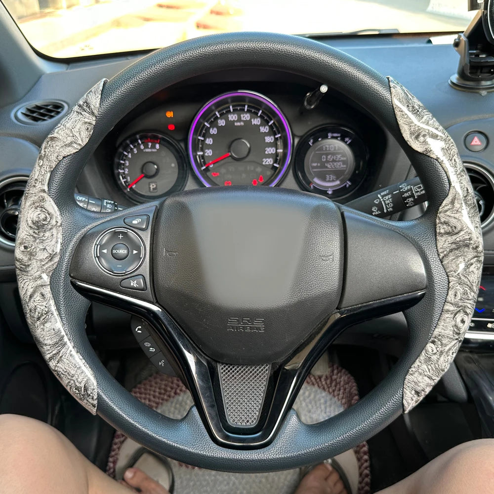 A close-up view of a black steering wheel with a patterned booster cover installed in a car interior.