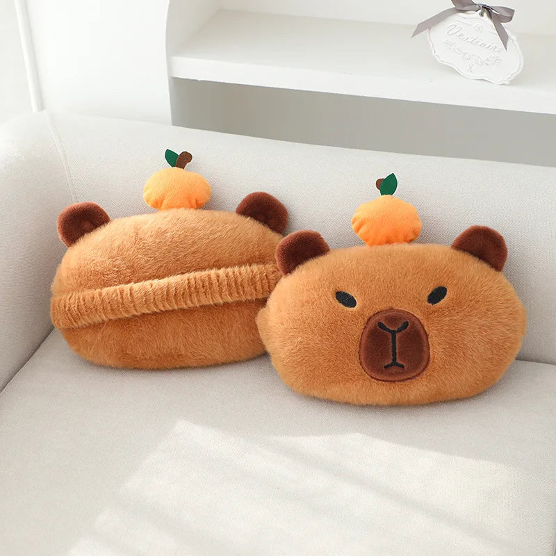 A fluffy orange plush capybara shaped like a bear is resting on a white sofa cushion.